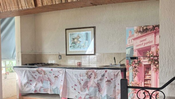 Et tekøkken med flisegulv, et bord med blomstret dug, et indrammet billede på væggen og en plakat med et bageri-motiv.
