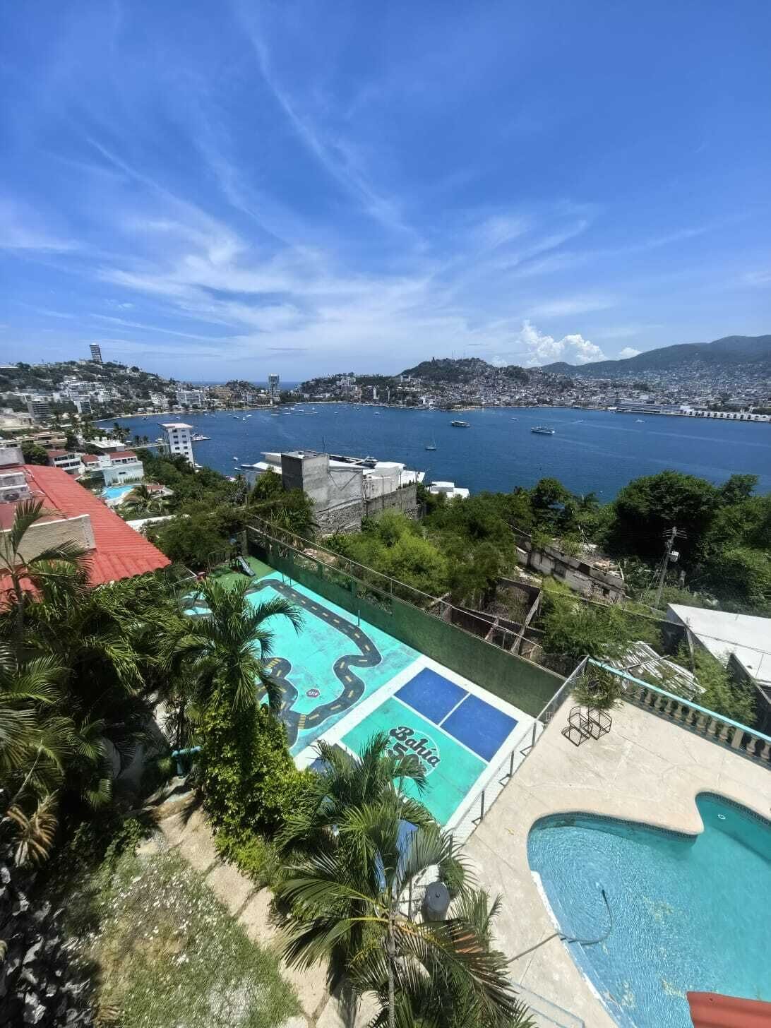 Un espace piscine offrant une vue sur le paysage urbain de la côte, avec notamment un port de plaisance et des collines à l’horizon.