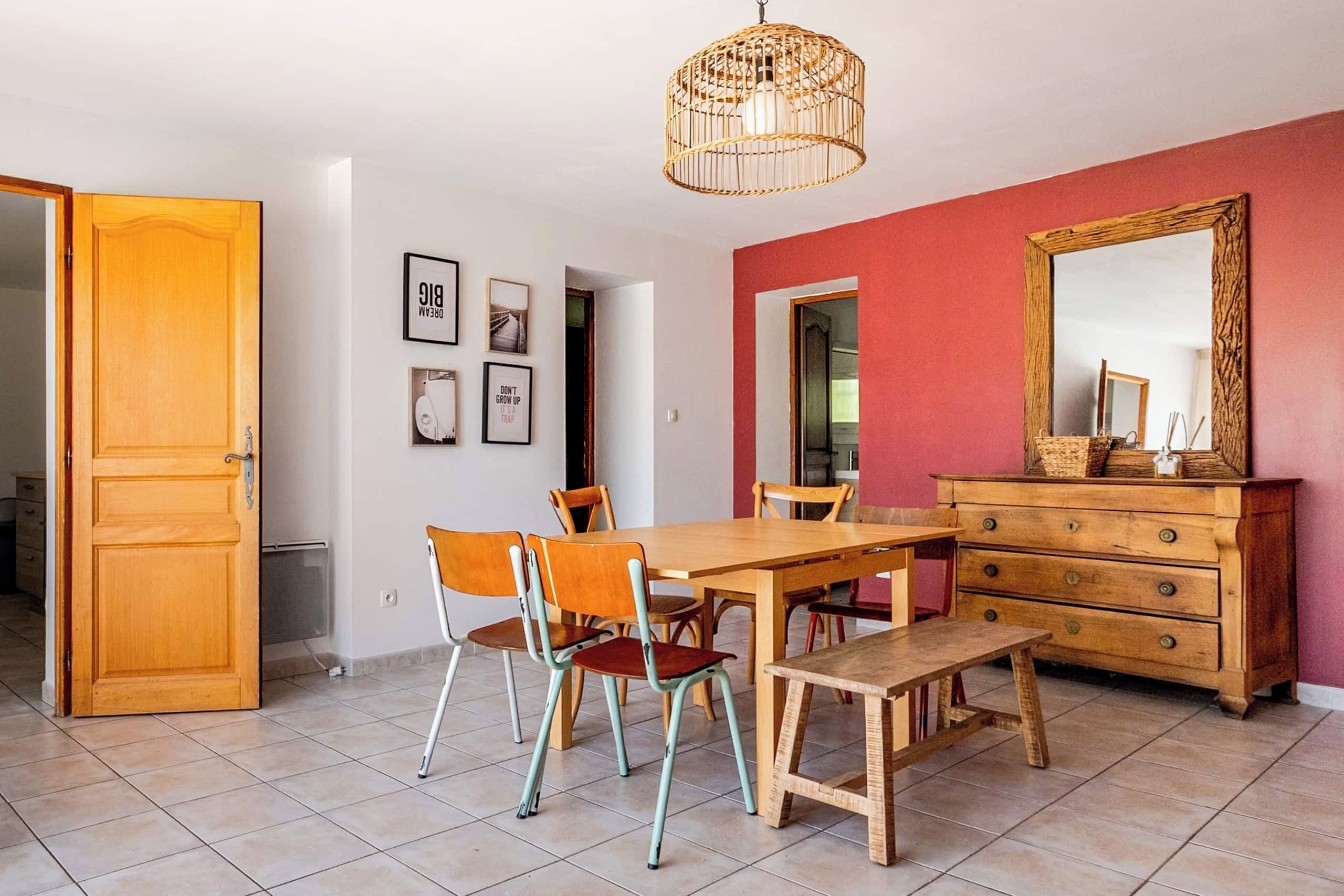 Un espace repas comprenant une table en bois, des chaises, un banc, une commode et un miroir.