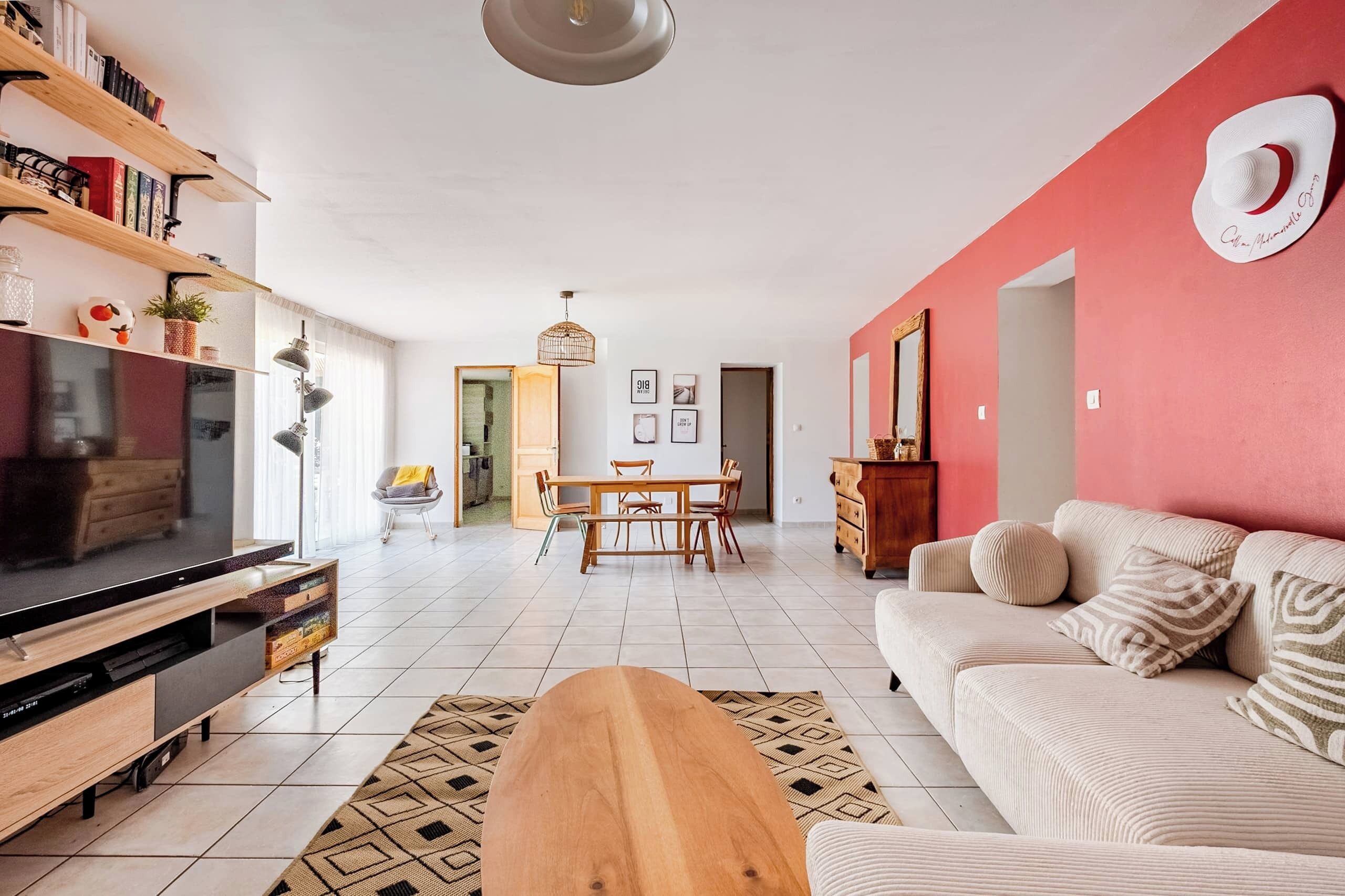 Sala de estar com televisão, móvel para TV em madeira, sofá e área de jantar com mesa e cadeiras.