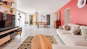 Una sala de estar con televisor, mueble de entretenimiento de madera, sofá y comedor con mesa y sillas.