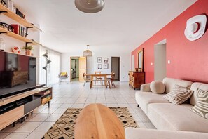 Ein Wohnzimmer mit Fernseher, einer Holzunterhaltungsecke, einer Couch und einem Essbereich mit Tisch und Stühlen.