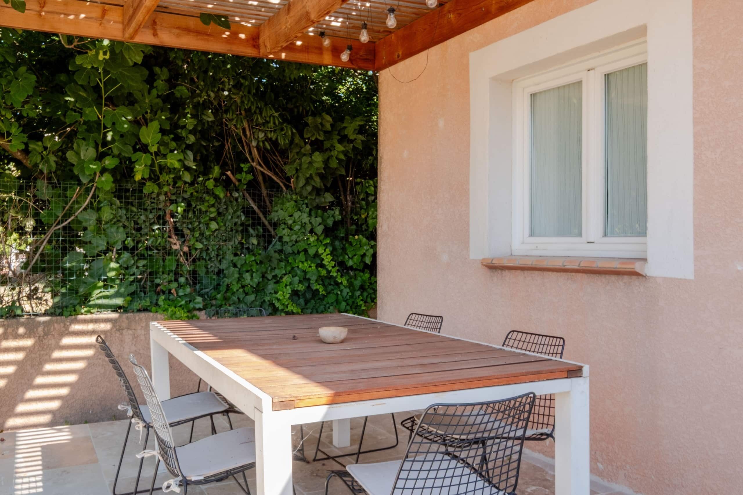 Une terrasse extérieure avec une table en bois et des chaises en métal, entourée d’un mur de verdure.