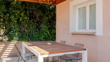 Une terrasse extérieure avec une table en bois et des chaises en métal, entourée d’un mur de verdure.