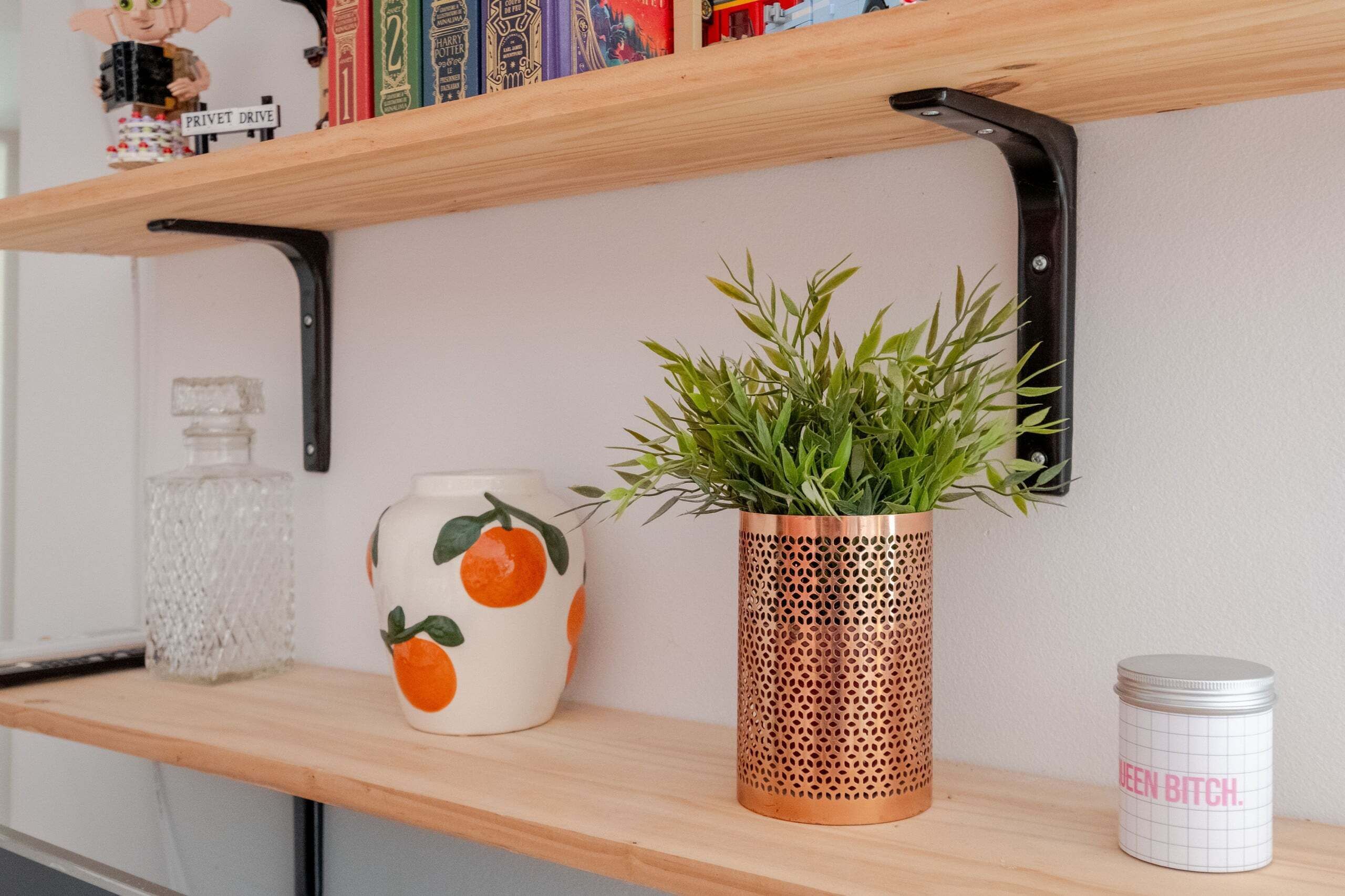 Une étagère avec une plante en pot, un vase en céramique orné de motifs orange et un récipient en métal avec du texte.
