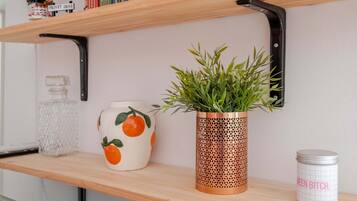 Une étagère avec une plante en pot, un vase en céramique orné de motifs orange et un récipient en métal avec du texte.