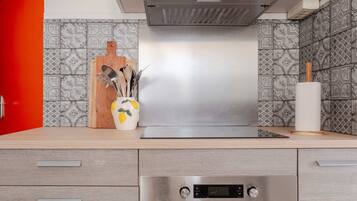 Une cuisine moderne dotée d’une hotte en acier inoxydable, d’une planche à découper en bois et d’un vase contenant des ustensiles de cuisine.