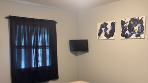 A bedroom with a bed, a window with curtains, a wall-mounted TV, and two abstract paintings. - 4-BR2-BA House INSIDE Iowa State fair! With jetted tub for 2 (Des Moines)