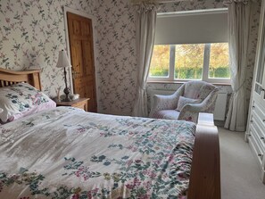 A bedroom with a floral-patterned bedspread, a wooden wardrobe, a chair with a floral cushion, and a window with curtains. - Golf enthusiasts- Gorgeous 4bedroom house in charming countryside. (Dromhane)