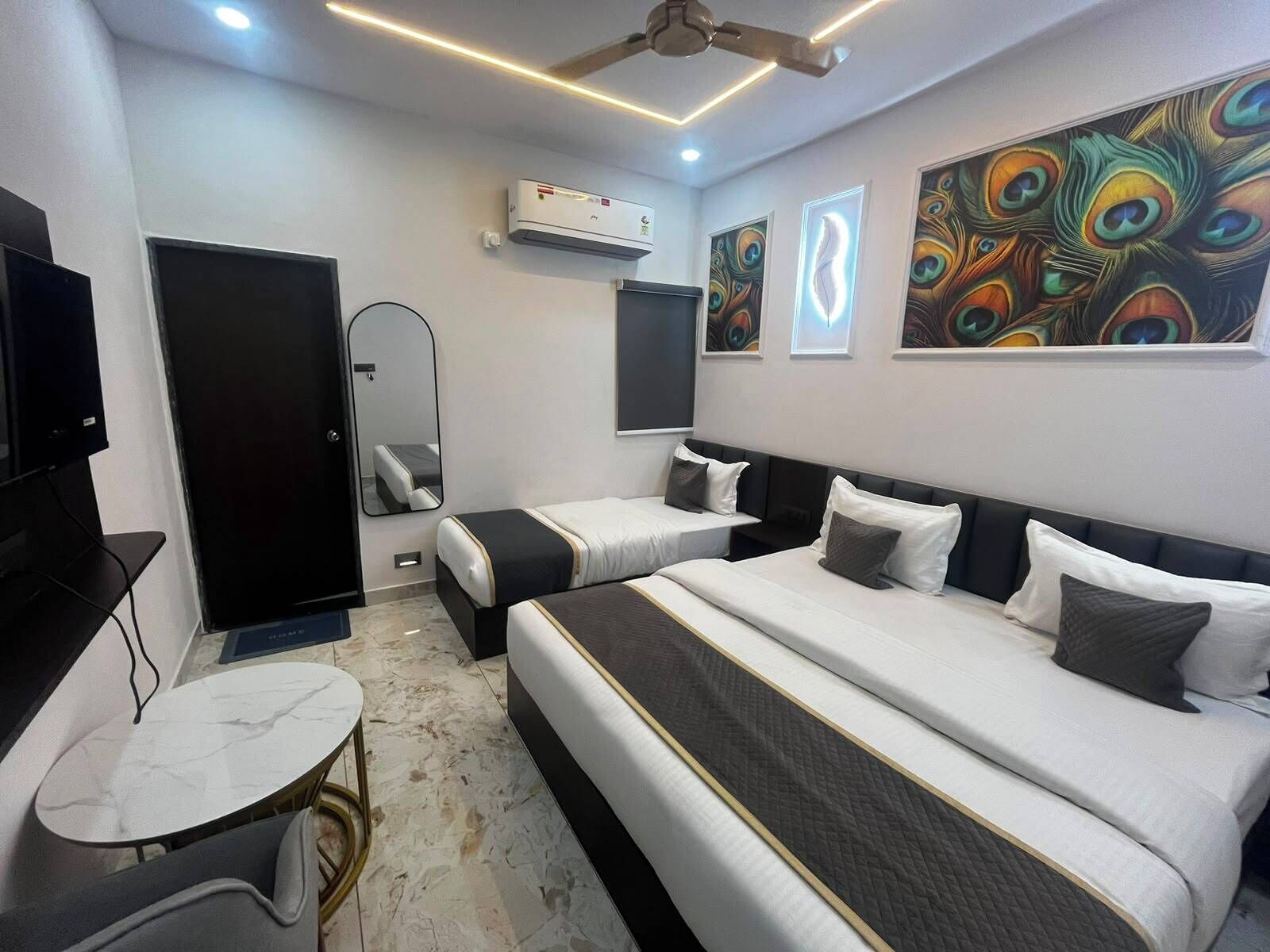 A hotel room with two beds, a desk, a mirror, an air conditioner, and peacock-themed wall art.