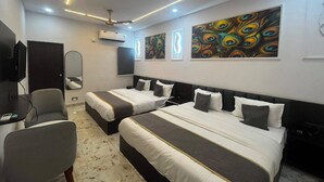 A hotel room with two beds, a desk, a chair, a ceiling fan, and artwork on the walls.