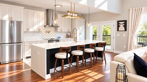 Une cuisine moderne dotée d’un îlot central, d’appareils électroménagers en acier inoxydable et de tabourets de bar en bois.