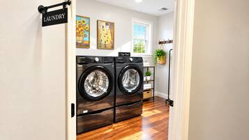 A laundry room with two front-loading washing machines, a wooden floor, and a window with a view of trees.