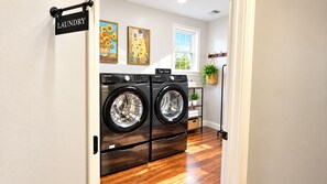 A laundry room with two front-loading washing machines, a wooden floor, and a window with a view of trees.