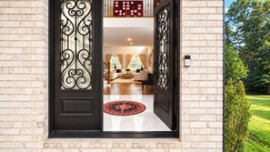 Une entrée moderne avec une porte noire et des éléments décoratifs en fer forgé, qui donne sur un intérieur bien éclairé, comprenant un canapé et une table basse.