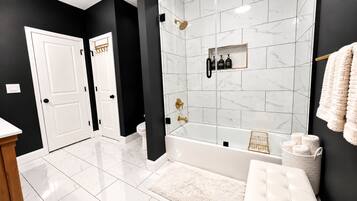 A modern bathroom with a bathtub, a shower, and a toilet. There are towels and toiletries on the wall.