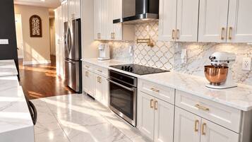 A modern kitchen with white cabinetry, stainless steel appliances, and a marble countertop.