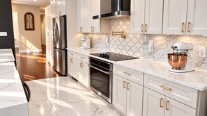 A modern kitchen with white cabinetry, stainless steel appliances, and a marble countertop.