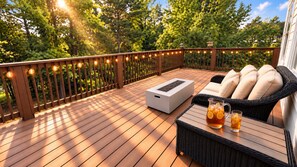 A wooden deck with a sofa and a table, surrounded by a wooden fence and string lights.