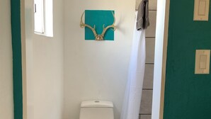 Ett litet badrum med en toalett, ett fönster, en duschdraperi och en väggdekoration i form av ett rådjurshorn.