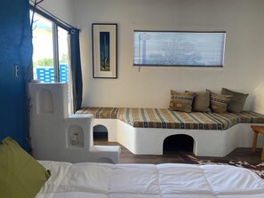 A bedroom with a bed, a window with blinds, a framed picture, and a built-in bench with cushions. - The Banco Room, a handcrafted Southwest retreat with  Adobe bancos & Kiva frplc (Tucumcari)