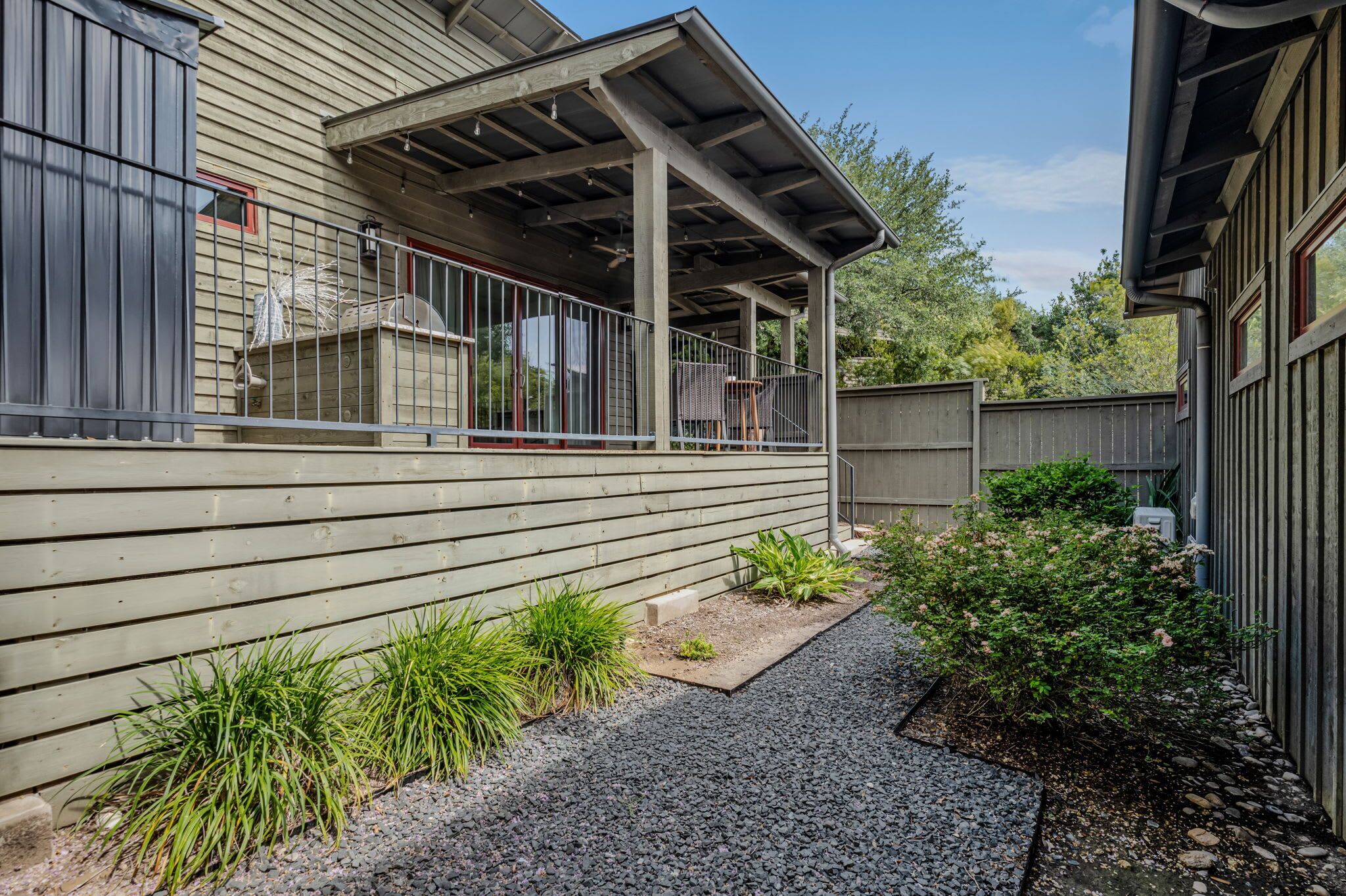 A covered outdoor area with a metal railing, a wooden fence, and a gravel path.