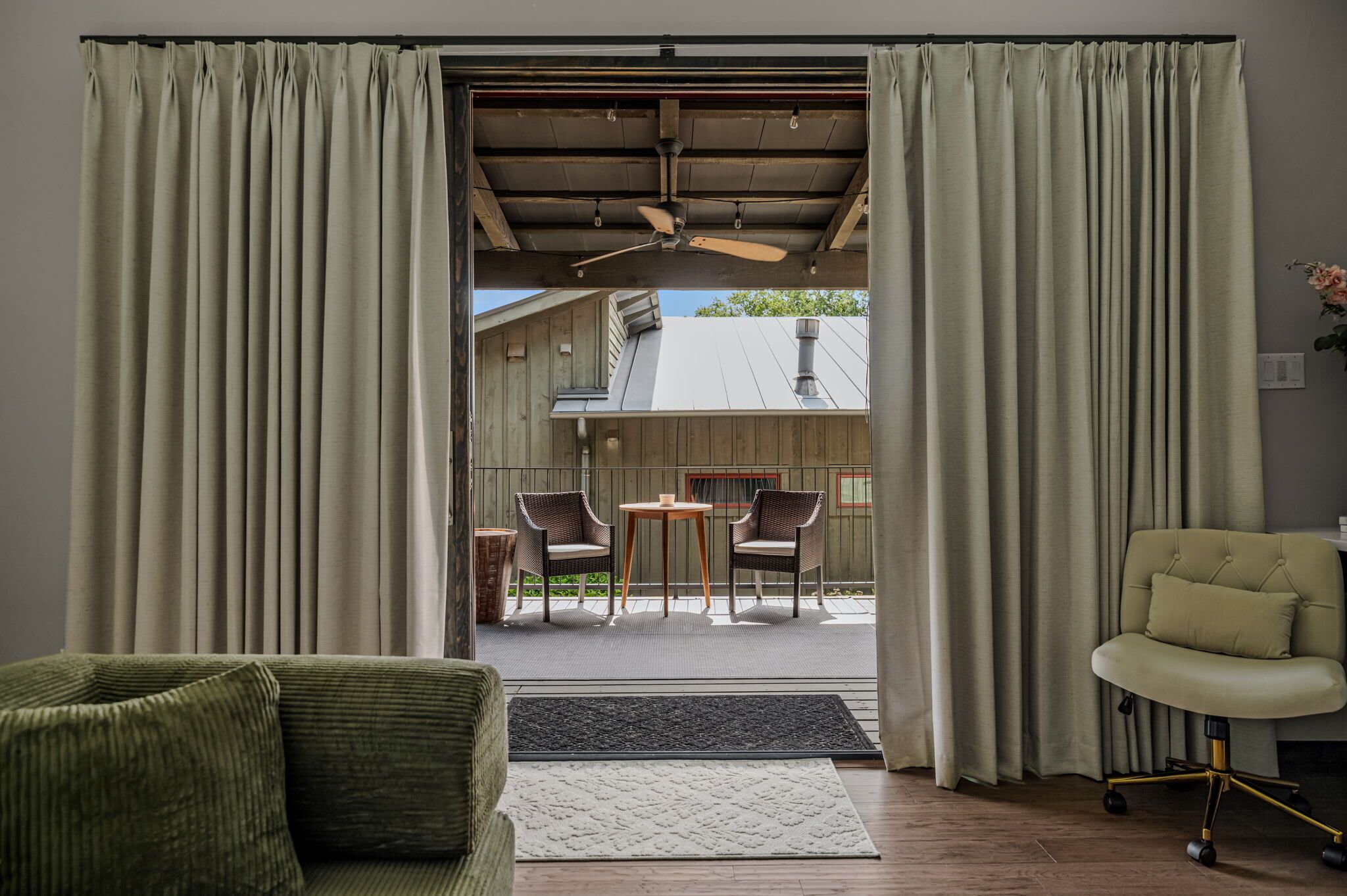 A room with a view of an outdoor patio, a ceiling fan, a green sofa, and a cushioned chair.