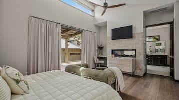 A bedroom with a large bed, a TV, a desk, and a bathroom.