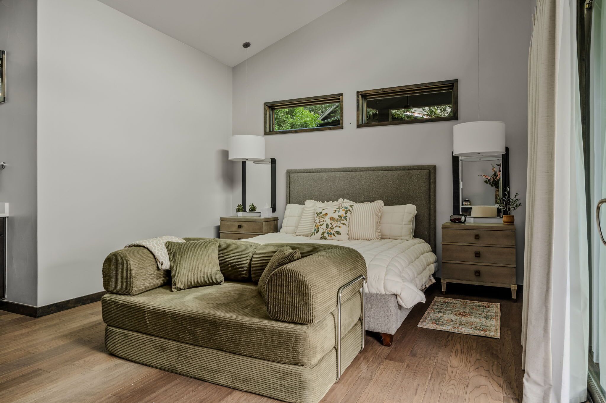 A bedroom with a bed, two bedside tables, a nightstand, a sofa, a window, and a mirror.