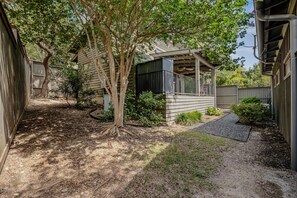 A residential property with a covered patio, a small garden area, and a dirt path leading to the house. - Charming Lakeside Cabin | BBQ Grill | Pickleball (Lake Travis)
