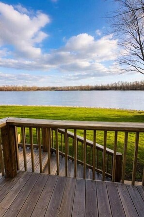 A wooden deck with a view of a lake and grassy area.