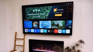 A flat-screen TV mounted on a wall above a fireplace, with a wooden ladder and a basket beside it.