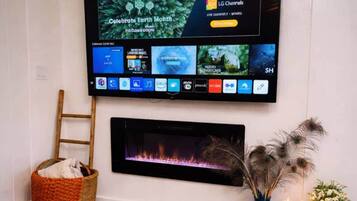 Ein Flachbildfernseher ist an einer Wand über einem Kamin befestigt, daneben steht eine Holzleiter und ein Korb.