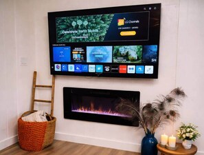 A flat-screen TV mounted on a wall above a fireplace, with a wooden ladder and a basket beside it.