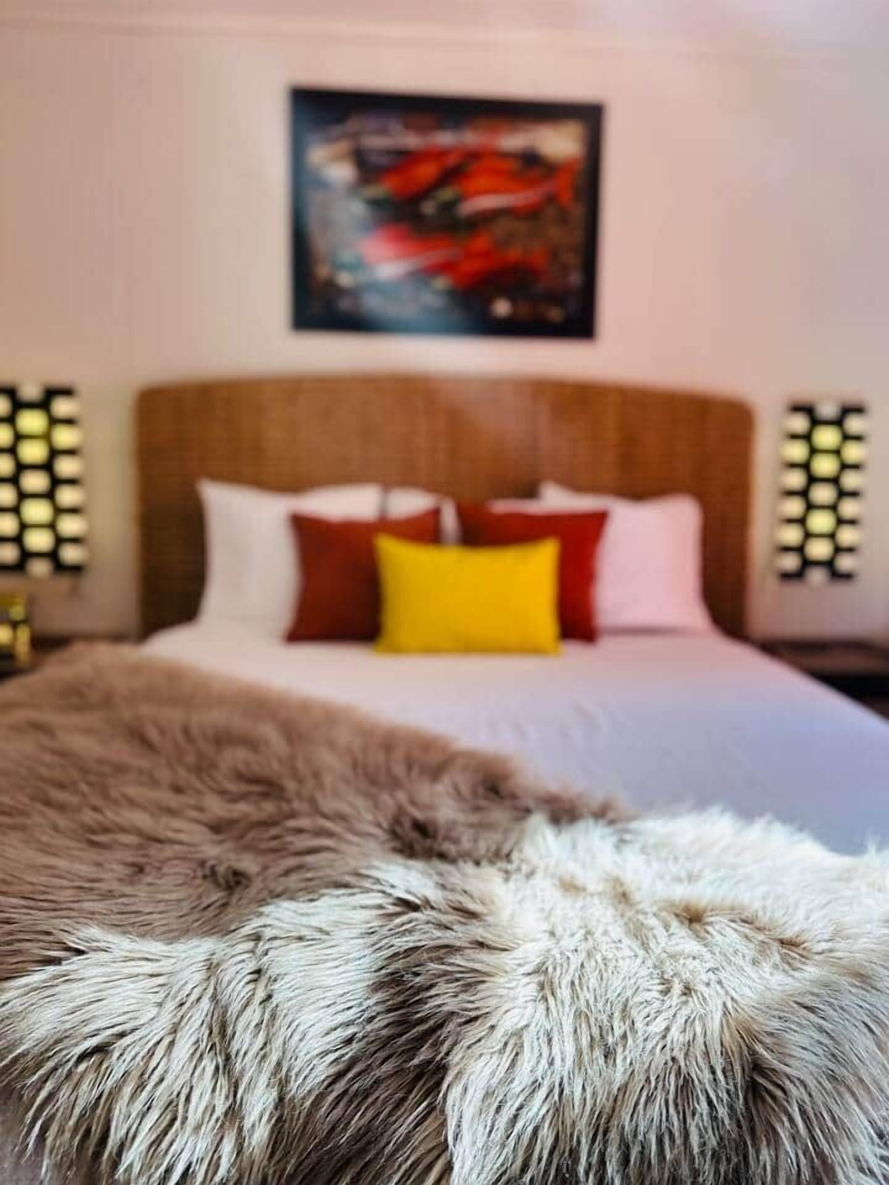 Una cama con cabecera de madera, almohadas blancas y rojas, y una manta de piel.