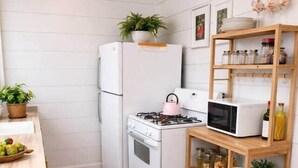 Une cuisine compacte équipée d’un réfrigérateur, d’une cuisinière, d’un four à micro-ondes et d’étagères en bois où sont rangés des bocaux et des assiettes.