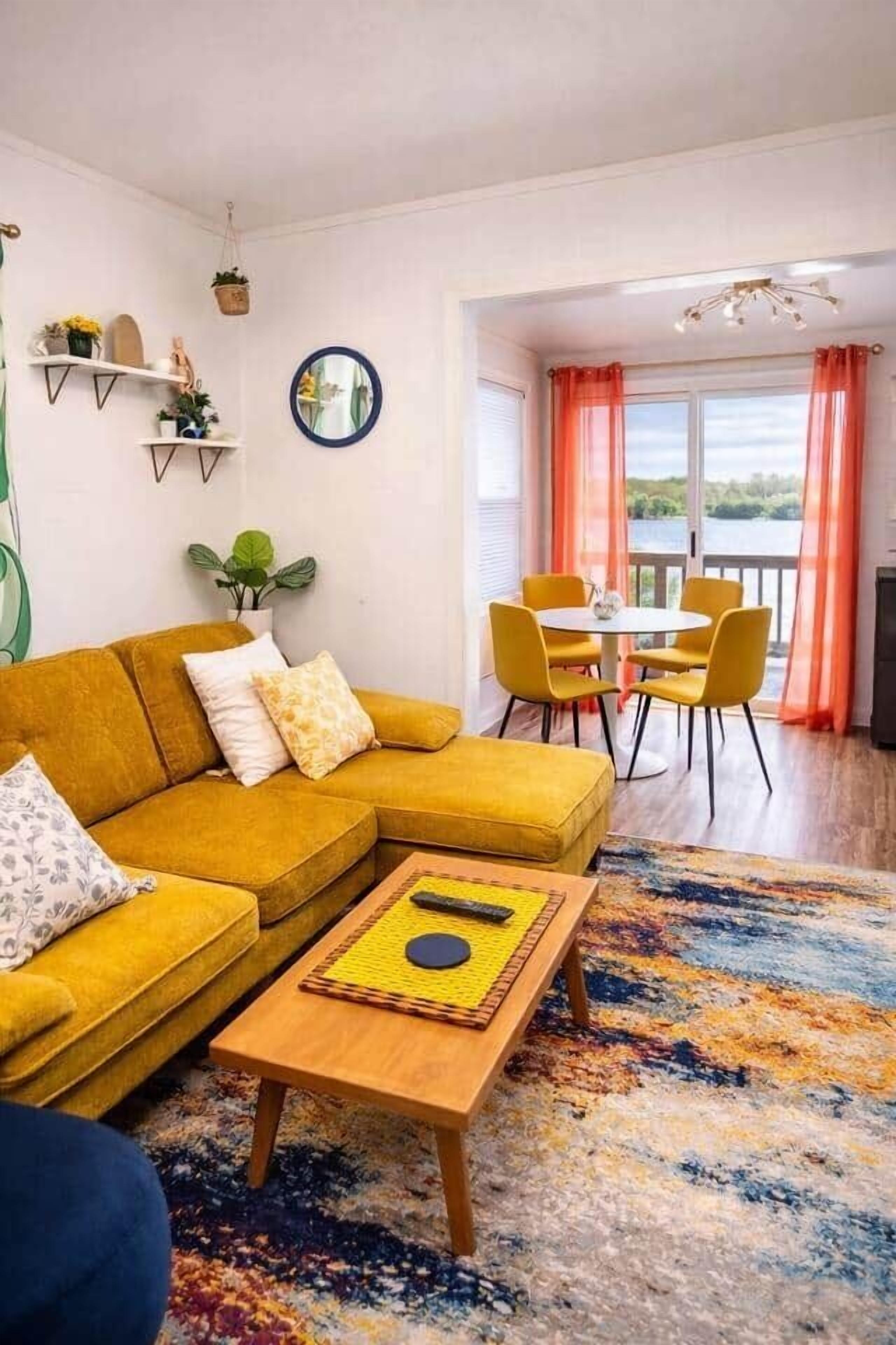 A living room with a yellow sofa, a coffee table, and a dining area with yellow chairs.