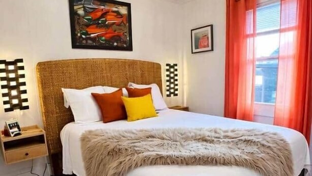 A bedroom with a large bed, a nightstand, a wall-mounted artwork, and a window with curtains.