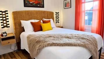 A bedroom with a large bed, a nightstand, a wall-mounted artwork, and a window with curtains.