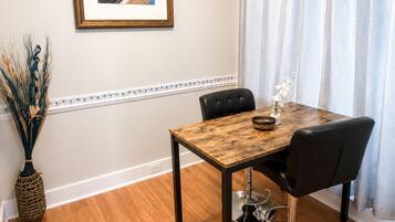 A dining area with a wooden table, black chairs, a framed picture on the wall, and a vase with dried plants.