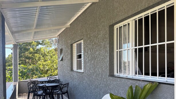 A covered patio area with a tiled floor, a table with chairs, a potted plant, and a window with bars. - Beautiful, fully equipped, and cozy country house for 10 people comfortably. (Salto de Pirapora)