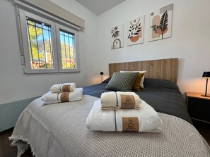 A bedroom with a bed, two pillows, a bedside table, a lamp, and a window with blinds.