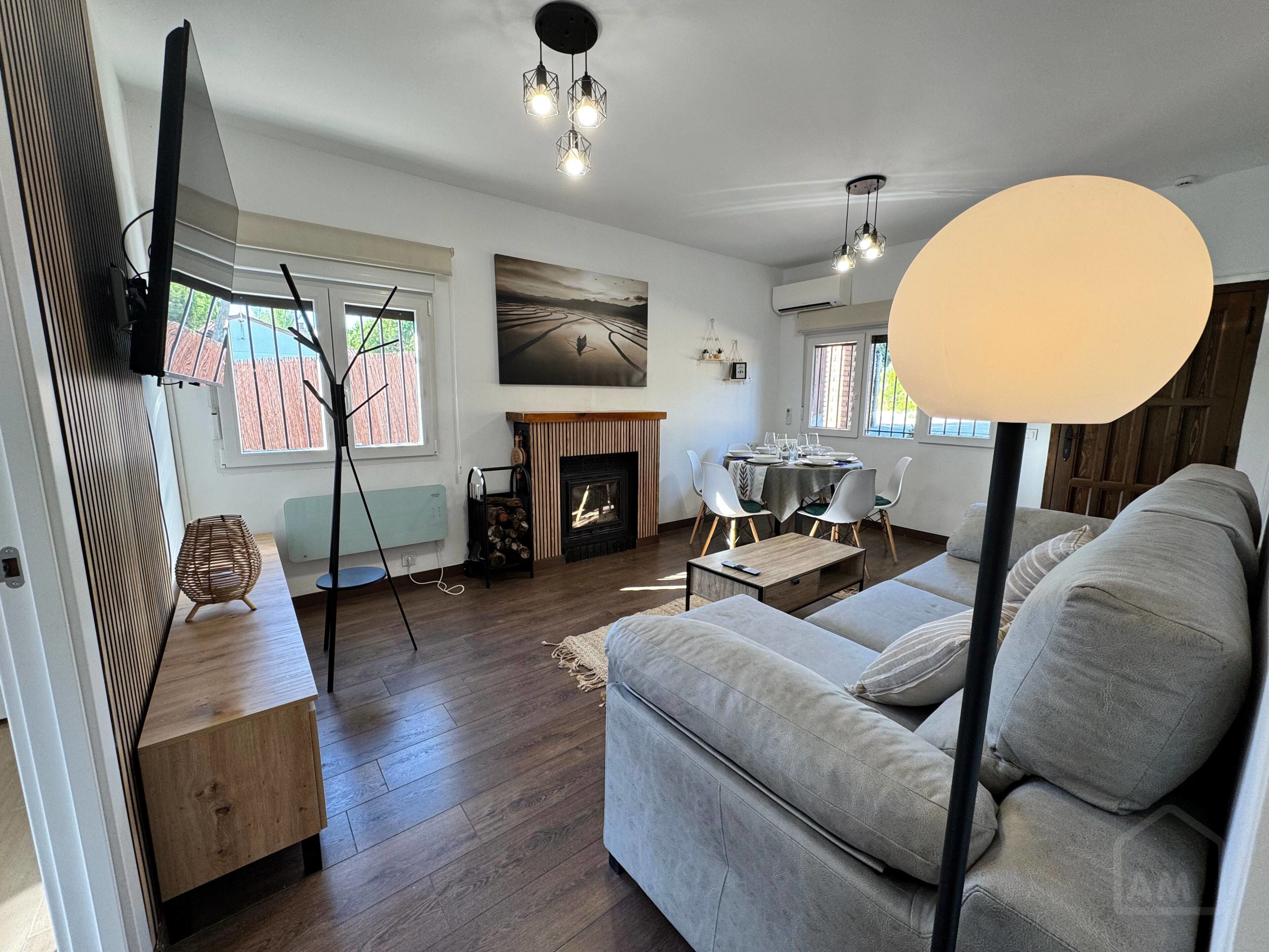A living room with a sofa, a fireplace, a dining table with chairs, and a TV mounted on the wall.