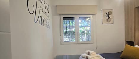 A room with a bed, a window, a wall with text, and a picture.