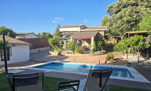 A backyard with a swimming pool, a patio with chairs, and a dining area. - Private chalet with pool, barbecue and fireplace, 1 hour from Madrid (Maello)