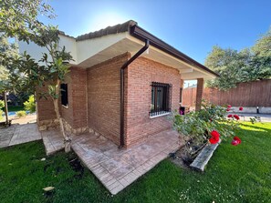 A brick house with a small porch, a window with bars, and a well-maintained lawn with red flowers.