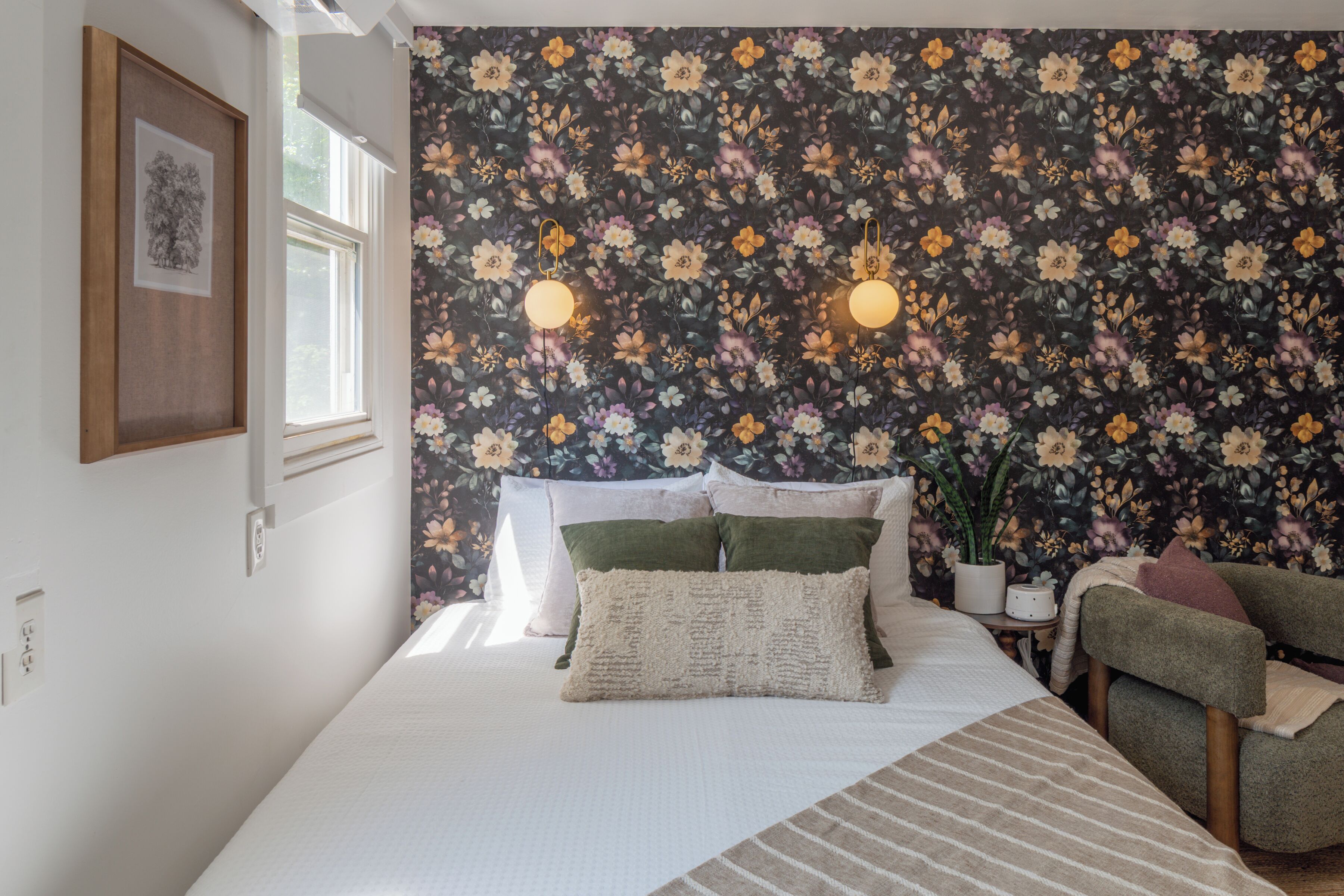 Une chambre à coucher avec un papier peint à motifs floraux, un lit avec des oreillers, une table de chevet avec une plante et une chaise.