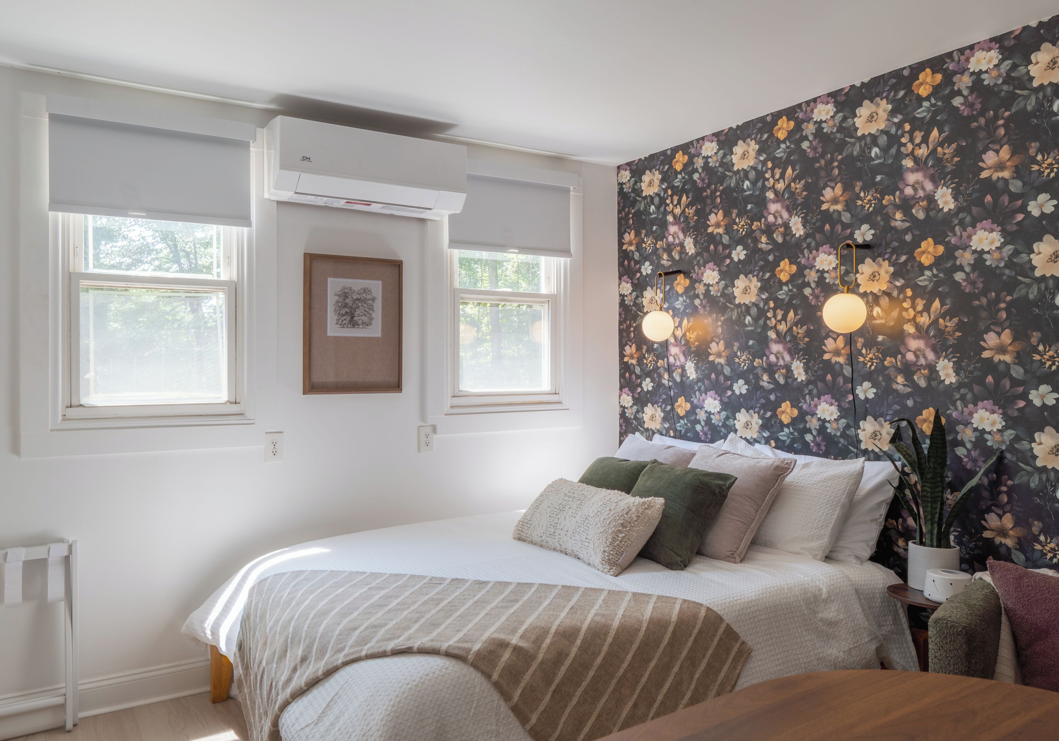 A bedroom with a bed, a window, an air conditioning unit, a wall-mounted light fixture, and a floral wallpaper.