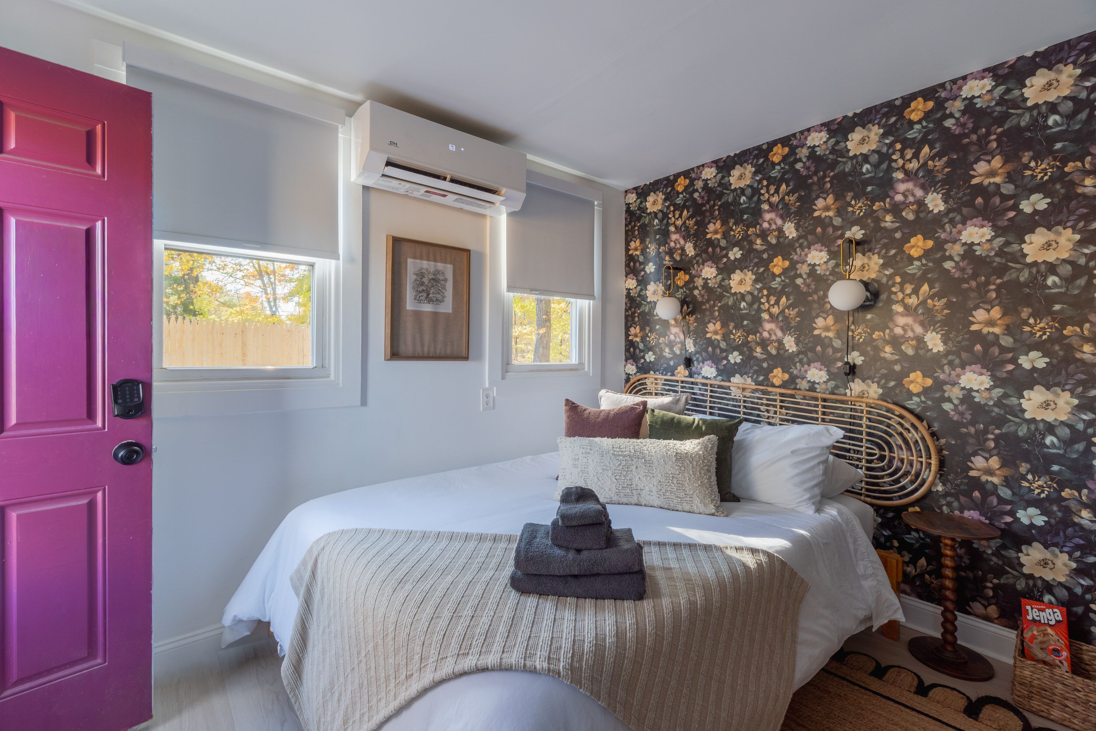 Een slaapkamer met een roze deur, een bed met wit beddengoed, bloemenbehang en een lijst met een afbeelding aan de muur.
