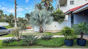 A residential area with a white building, a palm tree, and a car parked on the street. - SHB Condomínio com 5 Quartos e Lazer (Guarujá)